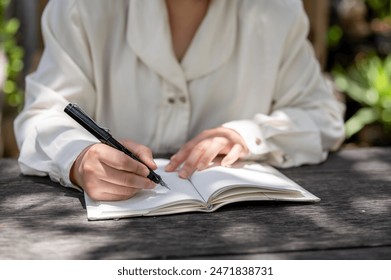 A cropped image of a woman writing something in a book or keeping her diary at a wooden table in a garden on a bright day. people and lifestyle concepts - Powered by Shutterstock