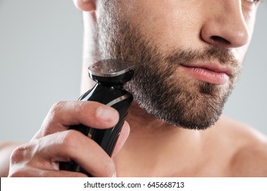 Cropped image of a young bearded man using electric shaver isolated over white background
