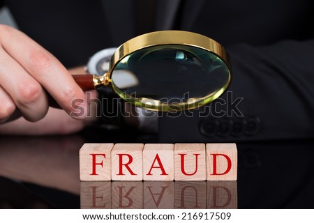 Cropped image of young businessman examining Fraud blocks through magnifying glass on desk