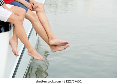 Cropped Image Of Young Couple Sitting On Yacht And Swinging Legs Over Water