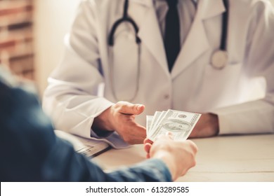 Cropped image of young doctor in white coat talking money from his patient while working in office