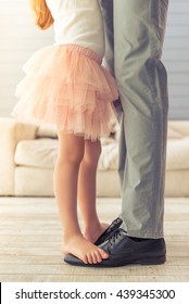Cropped image of young father and his cute little daughter dancing at home. Girl is standing on her father's feet