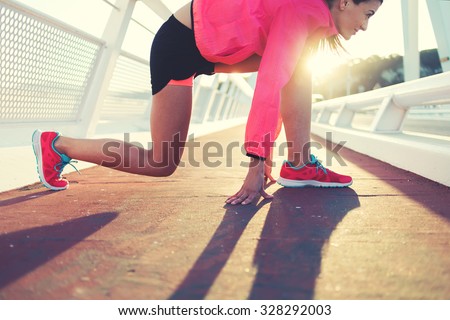 Cropped image of young fit woman in tracksuit took the position in preparation for her morning intense jog outdoors, sporty girl dressed in bright sportswear ready to start the run outside in evening