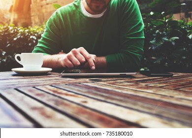 Cropped image young man sitting at the table with cup of coffee, digital tablet and smart phone, man's hands texting message on touch screen tablet while sitting on balcony terrace, flare sun - Powered by Shutterstock