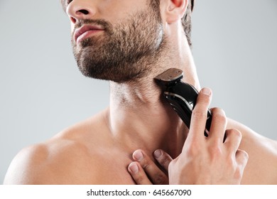 Cropped image of a young naked bearded man using electric razor isolated over white background - Shutterstock ID 645667090