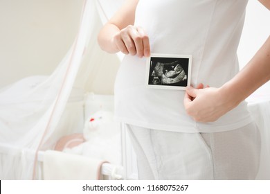  Cropped image of young pregnant woman holding ultrasound picture on belly. Concept of pregnancy, health care, gynecology, medicine. Mother waiting of the baby. Close-up.
