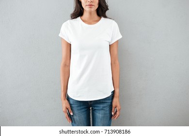 Cropped image of a young woman dressed in blank white t-shirt standing still standing isolated over gray background