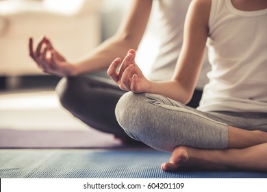 Cropped image of young woman and her little daughter doing yoga together at home