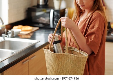 Cropped Image Of Young Woman Packing Bag For Picnic, She Is Putting Thermos In Straw Bag