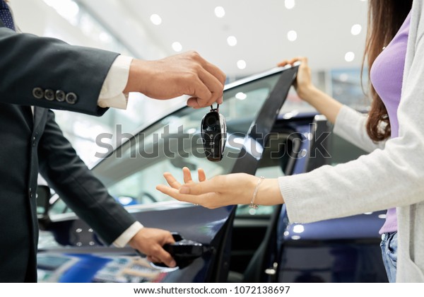 Cropped image of young woman receiving keys from her\
new car