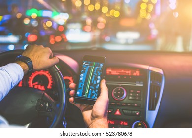 Cropped image.Closeup of smartphone in hand of young man sitting behind the wheel of modern car. In the background street lights and cars.Man paves way to browser. On screen of smartphone map of area