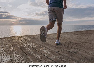 Cropped legs photo shot young strong sporty athletic fit sportsman man in sports clothes shorts warm up training jogging run at sunrise sun over sea beach outdoor on pier seaside in summer day morning - Powered by Shutterstock