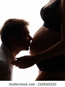 Cropped of loving man kissing belly of anonymous pregnant woman, with long pendant, wearing in black underwear, enjoying moment standing on white background