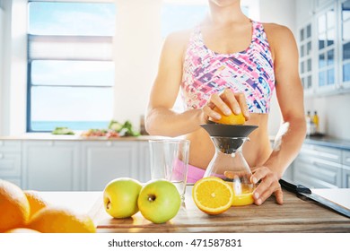 Cropped low angle view across the counter of a shapely fit healthy woman making fresh juice from apples and oranges using a manual blender with high key copy space on a window - Powered by Shutterstock