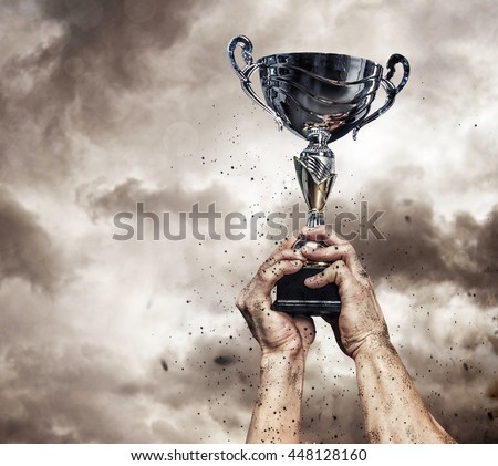 Cropped male arms with winner cup under cloudy sky.