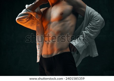 Cropped male body, muscular torso against dark textured studio background. Young man in white shirt and boxers. Concept of men's beauty, health, body art and aesthetics, care, sportive lifestyle