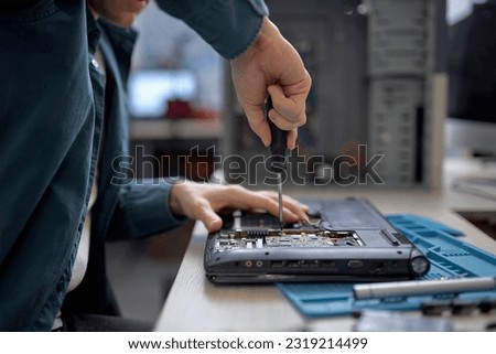 cropped male hands repairing parts in disassembled laptop using screwdriver and different tools on table in workshop. Hand technician repairing broken laptop notebook computer using tools