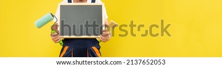 cropped man housepainter in work clothes hold paint roller brush and blackboard with copy space