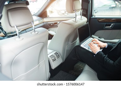 cropped man typing on laptop, using laptop while driving. very busy man sitting in luxurious car - Shutterstock ID 1576006147