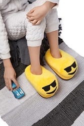 Cropped Medium Shot Of A Child In White Textured Pyjamas And Yellow Plush House Slippers Made As Cool Emoji In Sunglasses. The Child With A Blue Car Is Sitting On The Striped Carpet And A Gray Plaid.