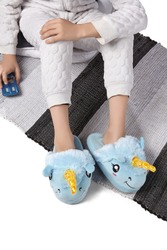 Cropped Medium Shot Of A Child In White Textured Pyjamas And Plush House Slippers Made As Blue Smiling Lamb Unicorn. The Child With A Blue Car Is Sitting On The Pillow And Striped Carpet.