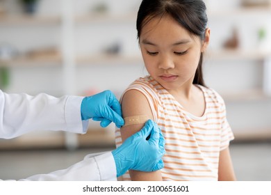 Cropped of nurse in protective gloves making vaccination against coronavirus of flu for chinese kid, applying adhesive band on shoulder, closeup shot. Kids immunization against various disease concept - Powered by Shutterstock