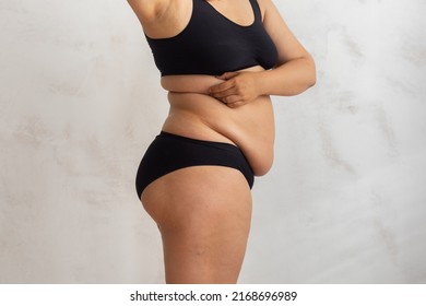 Cropped overweight fat woman pinching and checking volume of sides in black bikini. Excess skin problem after childbirth. Edema fibrosis skin. Loosing skin turgor. Emphasizing adiposity. Side view