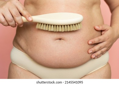 Cropped overweight woman belly with navel in pants with excessive weight, visceral fat abdomen. Brush dry massage by natural stubble, rubbing. Making skin elastic, get rid of hanging tummy. Home spa