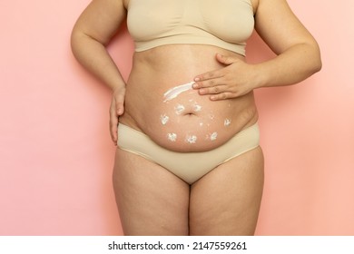 Cropped overweight woman in underwear applying moisturizer cream lotion to her abdomen. Fat removal. Wearing underwear, doing self massage to puffy skin. Cellulite obesity. Postnatal, body positive