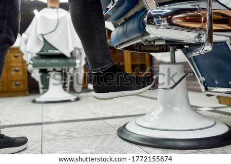 Cropped photo of adjustable barber chair. Barber adjusting barber chair while working in the modern barbershop. Selective focus, close up. Hair salon. Barbershop concept