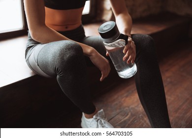 Cropped Photo Of Attractive Fitness Woman Sitting In Gym And Holding Bottle Of Water.