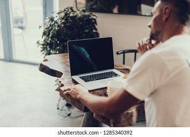 Cropped photo of blurred mature man sitting in cafe behind wooden table. Selective focus on laptop with empty display and copy space for text - Shutterstock ID 1285340392