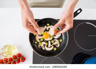 Cropped photo cooking man adding sliced vegetables mushrooms on frying pan making omelette