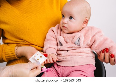 Cropped Photo Of A Cute Baby In Mummy Arms Choosing Golden Small Medical Earrings For Ear Piercing. White Background.