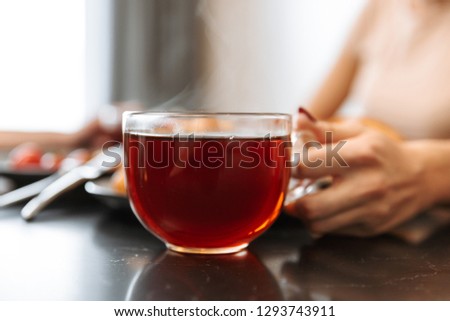 Cropped photo of european woman sitting at table in flat with hot tea in glass
