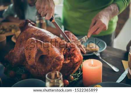 Cropped photo of family feast roasted turkey on table grandfather hands cutting meat into slices hungry relatives waiting in living room indoors