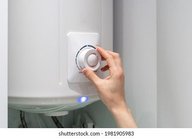 Foto recortada de una hembra ajustando la temperatura en la caldera eléctrica del baño colgando de la pared, usando el botón de control. Calentador de agua en apartamento moderno