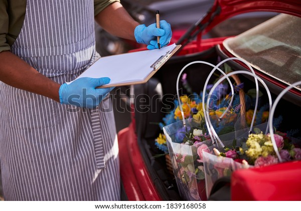 Cropped photo of a\
florist store worker in blue gloves holding his pen ready for\
writing down the\
information