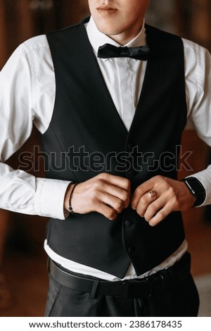 Cropped photo of groom in white shirt buttoning black vest. Business style. A stylish watch