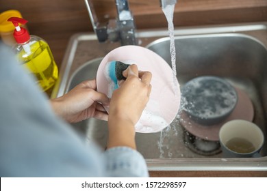 Cropped photo of hands cleaning a plate with dishwashing soap - Shutterstock ID 1572298597