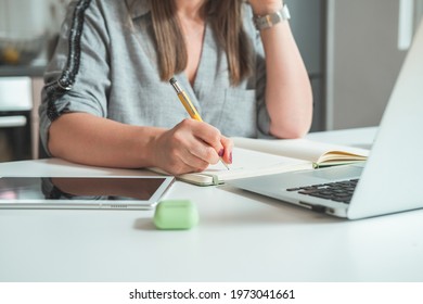 Cropped Photo of Businesswoman Working at Home Office Desk.
Unrecognizable business woman talking with coworkers on video call and writing down notes in notebook while sitting at desk with copy space.