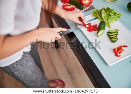 Cropped photo of a lady cutting a sweet pepper in small pieces on a plastic board