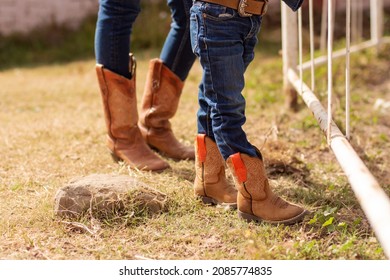 Cropped photo of the legs of a woman and child wearing jeans and cowboy boots on a ranch