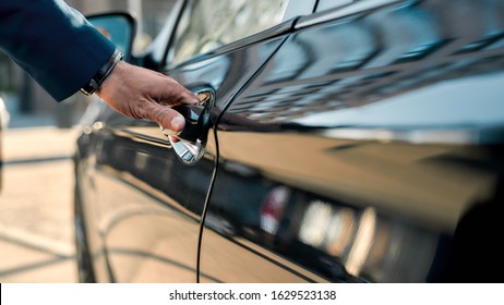 Cropped photo of a male hand opening the door of a black car while standing outdoors. Close up. Transportation
