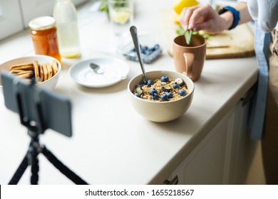 Cropped photo of mother holding baby while using smartphone for blog in the kitchen stock photo - Shutterstock ID 1655218567