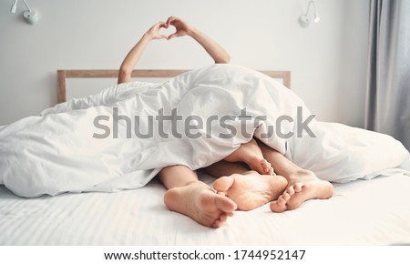 Cropped photo of newly wedded couple making a heart shape with their hands in bed