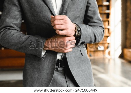 Cropped photo of prosperous businessman touching his sleeves of tuxedo in office. Manager boss millionaire fixing formal suit attire at workplace. Expensive wristwatch