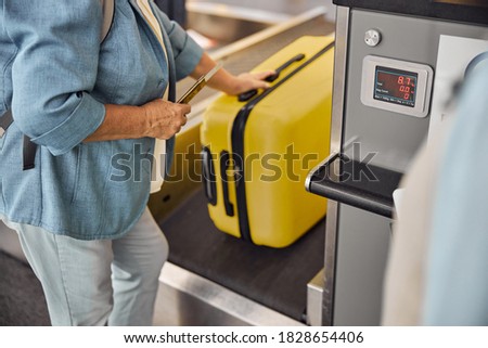 Cropped photo of a senior Caucasian female passenger placing her bag on the conveyor belt