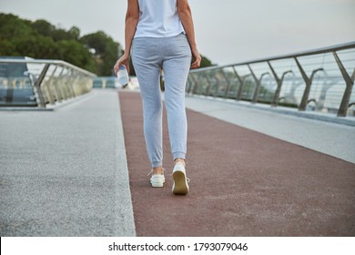Cropped photo of a slim Caucasian woman in sweatpants and sneakers treading the bridge outside