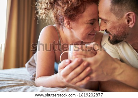 Cropped photo of smiling lovely couple with coffee lying in bed stock photo
